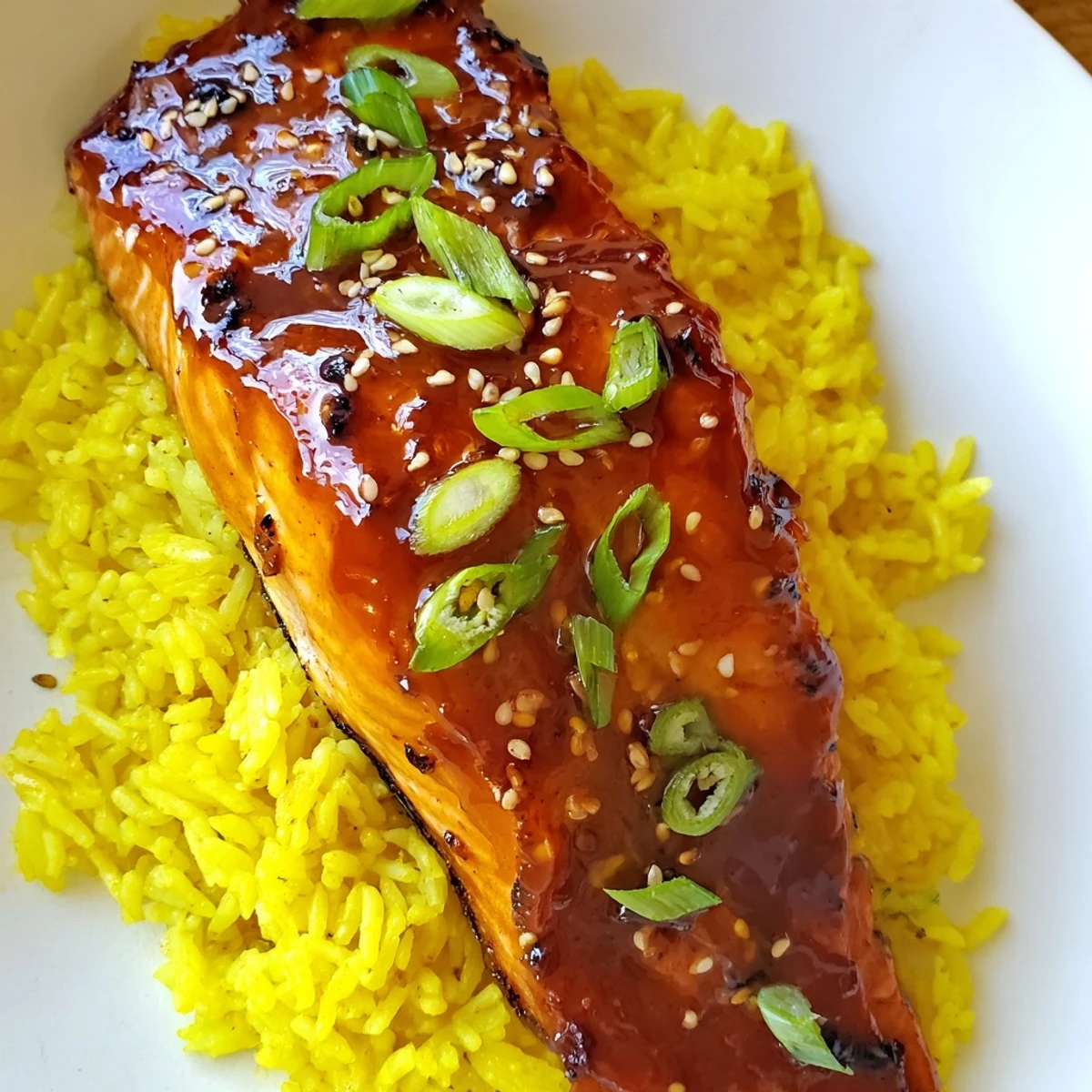 A close-up of tender, caramelized Sticky Orange Salmon atop a mound of creamy rice, ready to eat.
