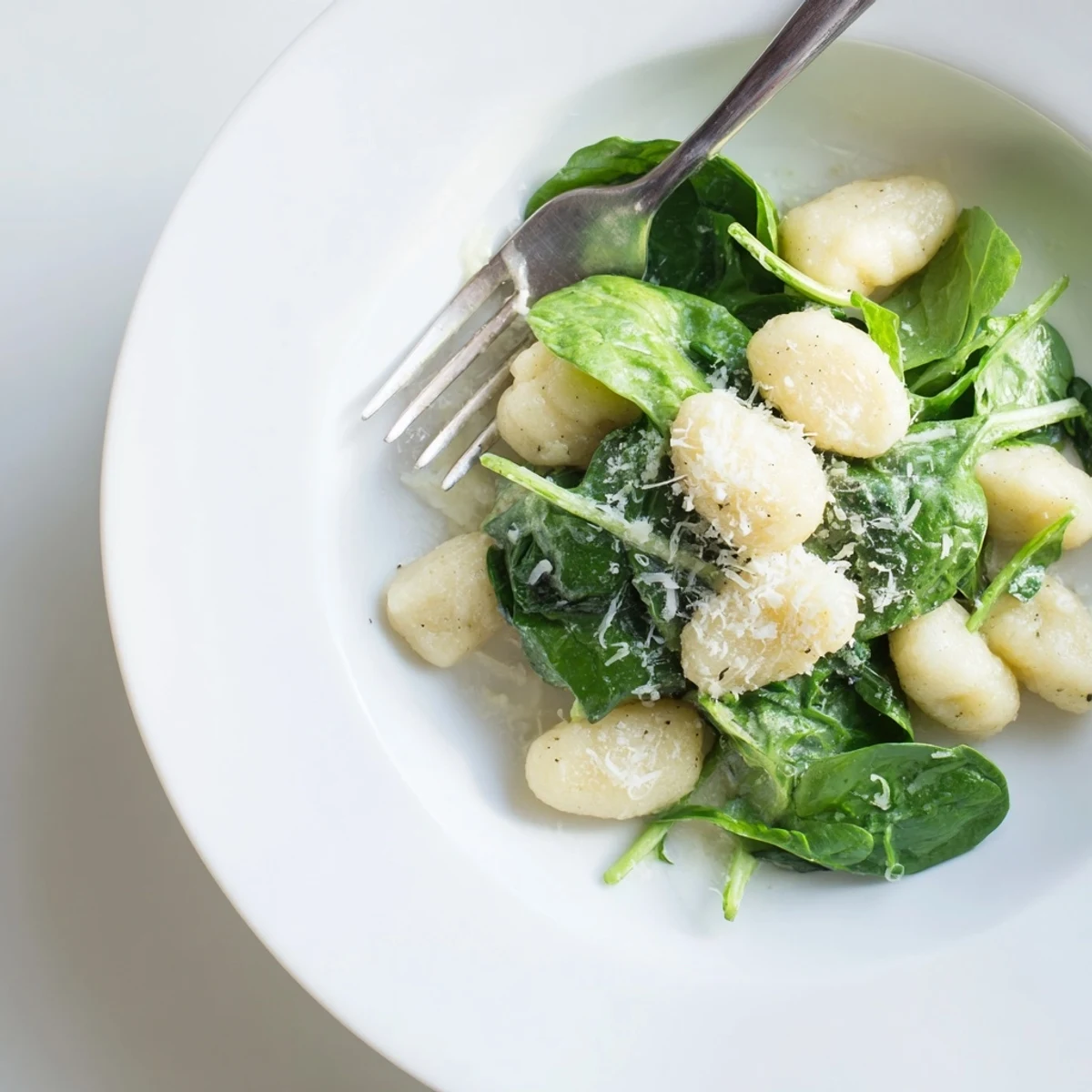 A close-up of Creamy Garlic Gnocchi, highlighting the glossy Parmesan sauce clinging to each pillow, garnished with fresh black pepper.