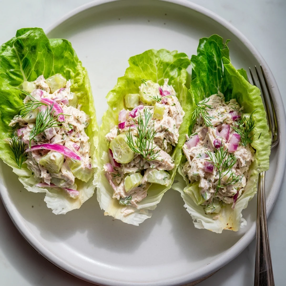 Overhead shot of Dill Pickle Chicken Salad Lettuce Cups arranged on a white platter, highlighting the vibrant textures of the tangy salad filling contrasted against the delicate, cupped leaves.