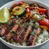 Golden-brown steak and colorful roasted vegetables rest on a bed of fluffy rice, garnished with fresh parsley and lemon wedges.  