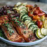 Golden-brown roasted salmon fillets nestled among vibrant red bell peppers, zucchini, and cherry tomatoes on a sheet pan, garnished with fresh parsley.  