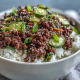 Top-down view of a Korean Ground Beef Bowl with seasoned beef, fluffy rice, and colorful quick-pickled vegetables like carrots and cucumbers.