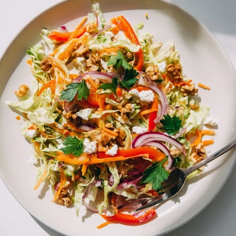 A close-up of warm sautéed cabbage salad tossed with crisp carrots, red onion, and bell peppers, topped with crumbled feta and toasted walnuts.