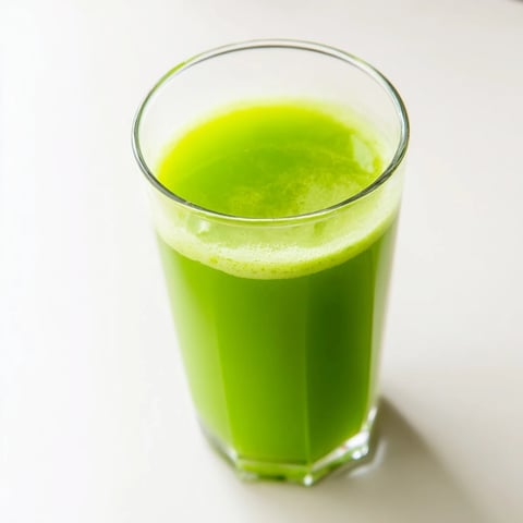 Freshly blended Cabbage and Kale Detox Juice poured into a glass with ice cubes, featuring vibrant green hues from kale and celery with a slice of lemon garnish. 