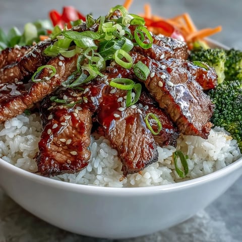Steak and vegetables coated in glossy teriyaki sauce served over fluffy white rice in a bowl.