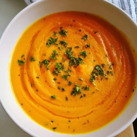 Vivid orange puree of roasted carrots and ginger in a white bowl, evoking a cozy, vegetarian dinner in the kitchen.