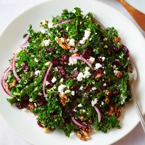 Warm Kale Salad with Maple Mustard Dressing topped with crumbled feta, toasted pecans, and dried cranberries on a rustic wooden board.
