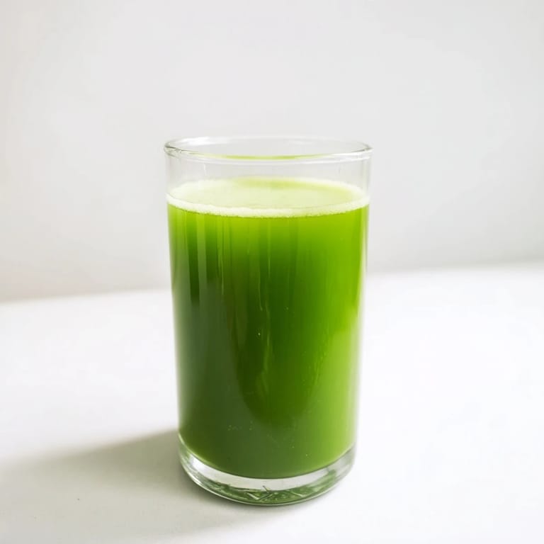 Clear glass pitcher of Cabbage and Kale Detox Juice with visible pulp, surrounded by chopped green apples and cucumbers on a marble countertop.