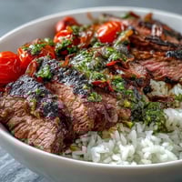 Tender grilled steak slices over fluffy rice and roasted veggies, all topped with vibrant green chimichurri sauce for a colorful Grilled Steak Bowl.